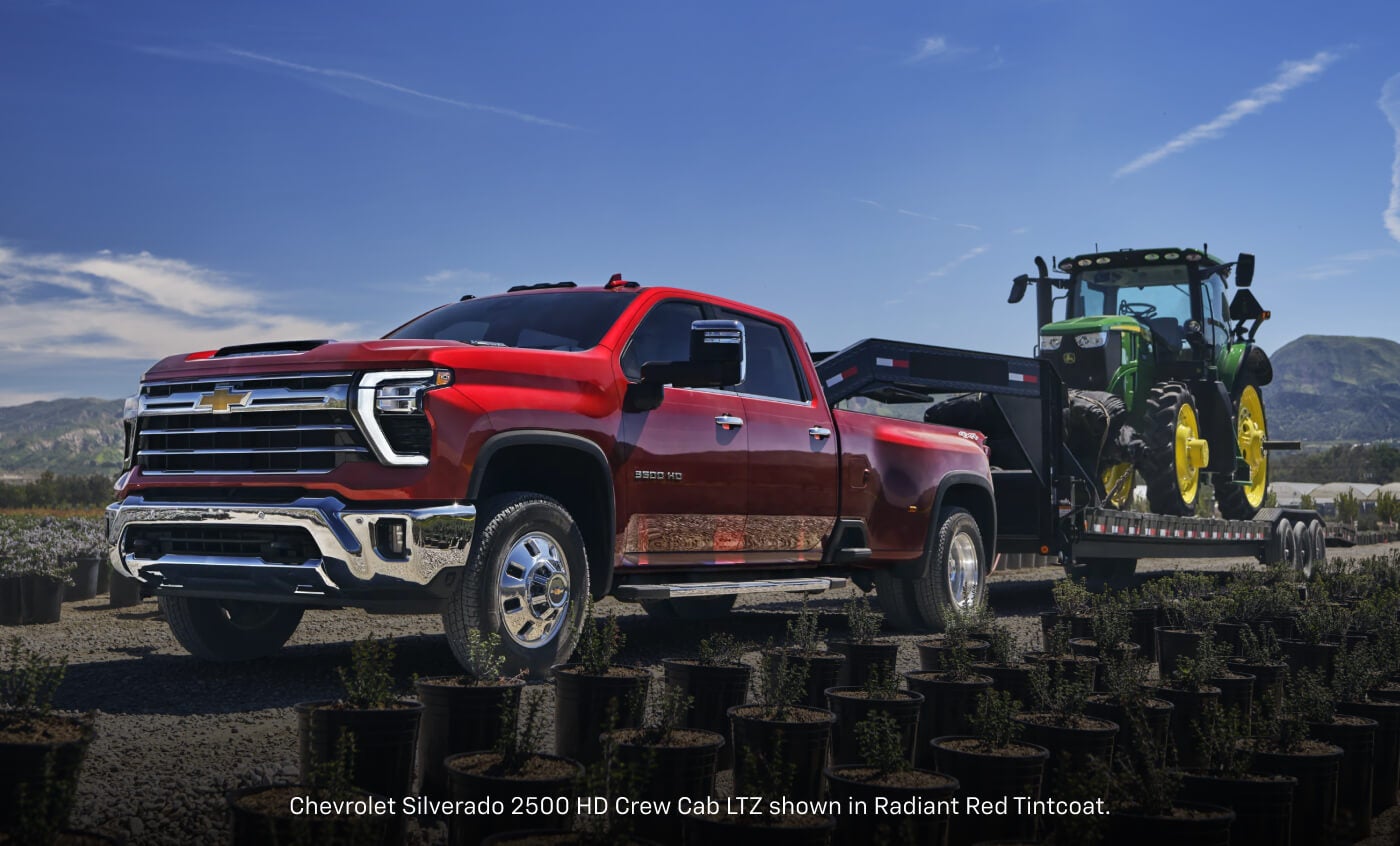 Front three-quarter view of a 2026 Chevrolet Silverado 2500 HD LTZ Crew Cab in Radiant Red Tintcoat towing a heavy-duty gooseneck.