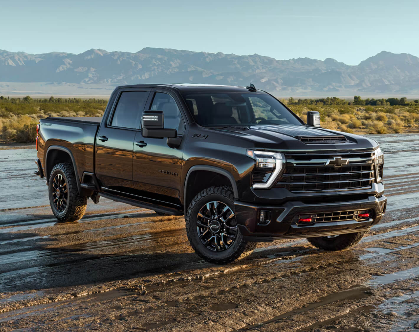 A Black Chevrolet Silverado HD Stars and Steel Edition Truck on a Wet Dirt Road with Mountains.