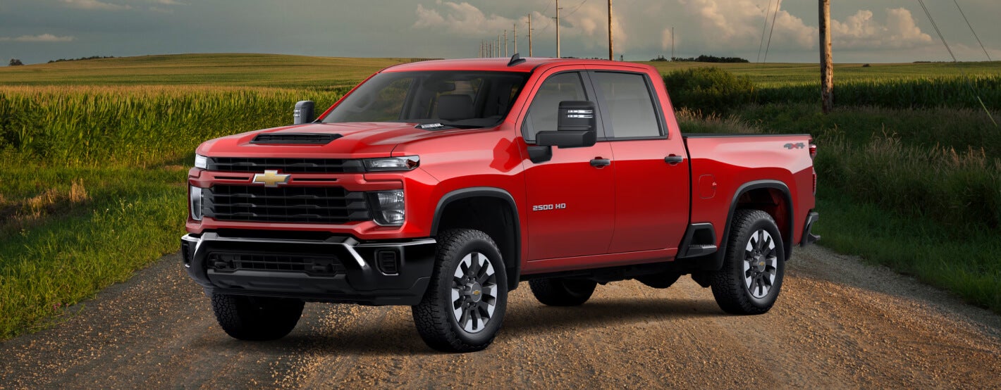 Side view of the 2026 Silverado 2500 HD Custom in Radiant Red Tintcoat on a grassy road.