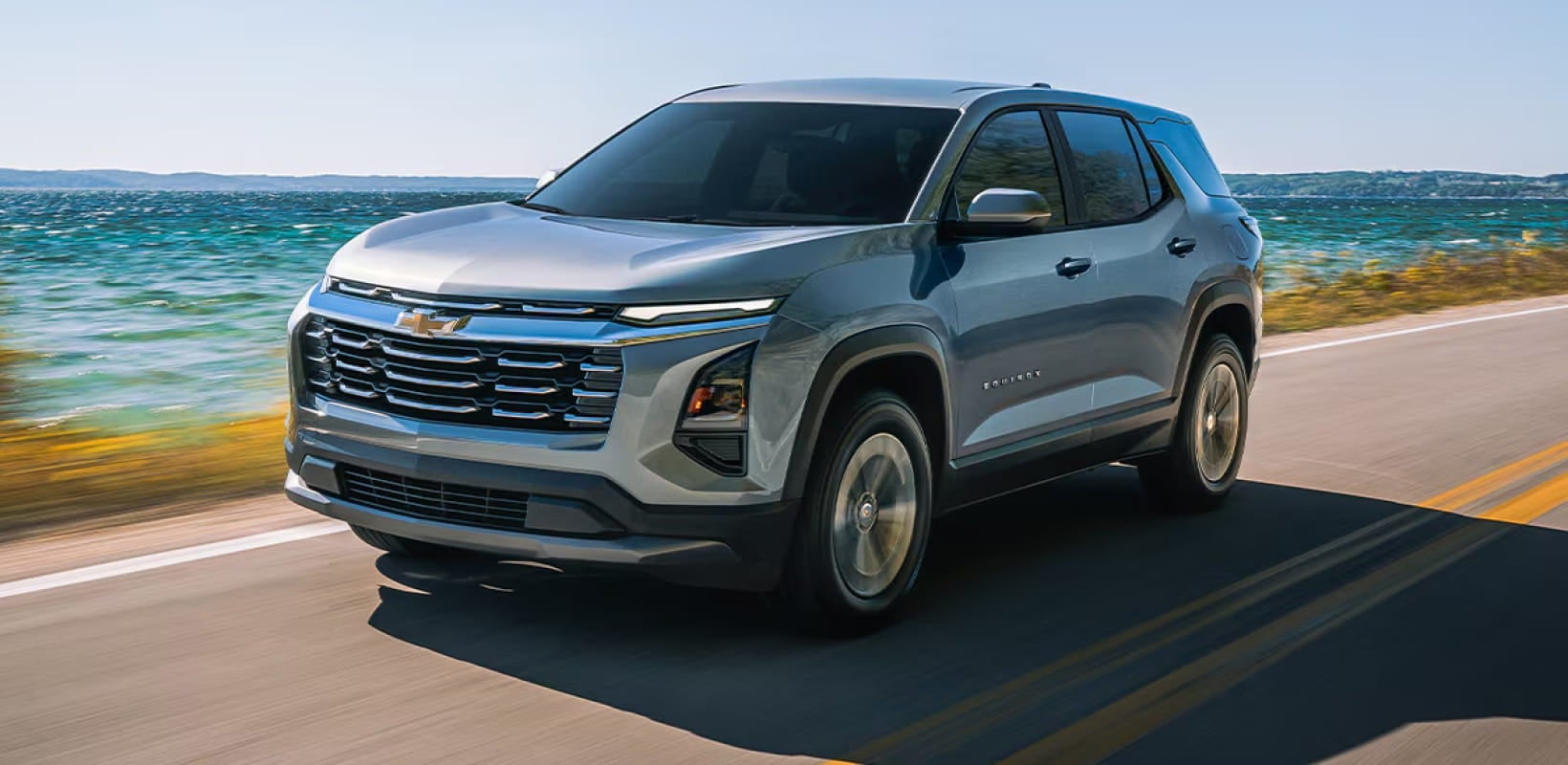 Gray Chevrolet Equinox driving along a scenic waterfront road.
