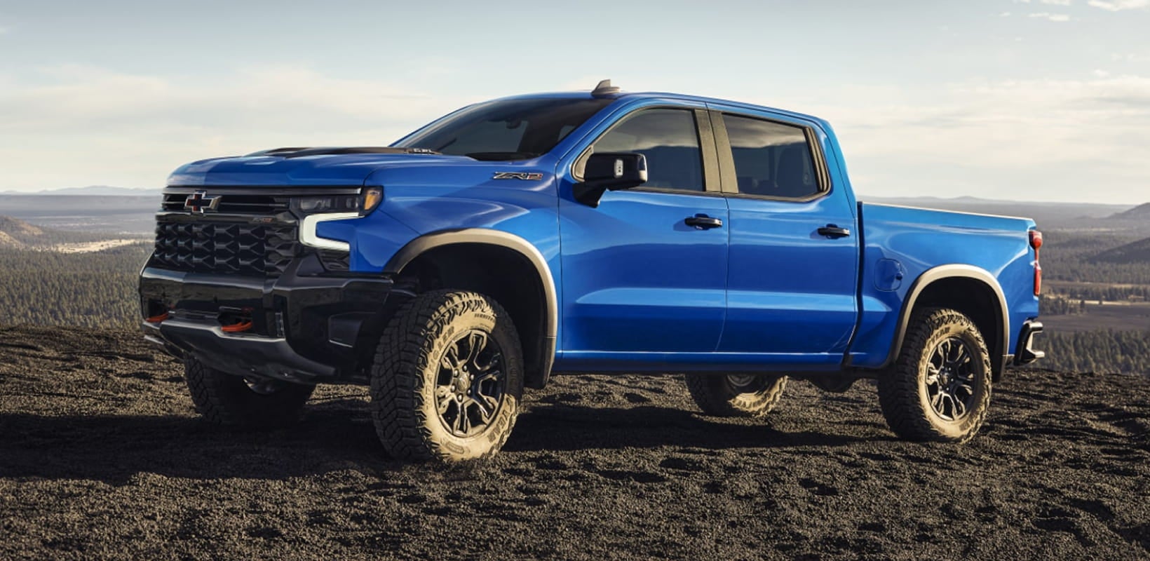 Blue Chevrolet Silverado parked on rugged terrain with a mountain landscape in the background.