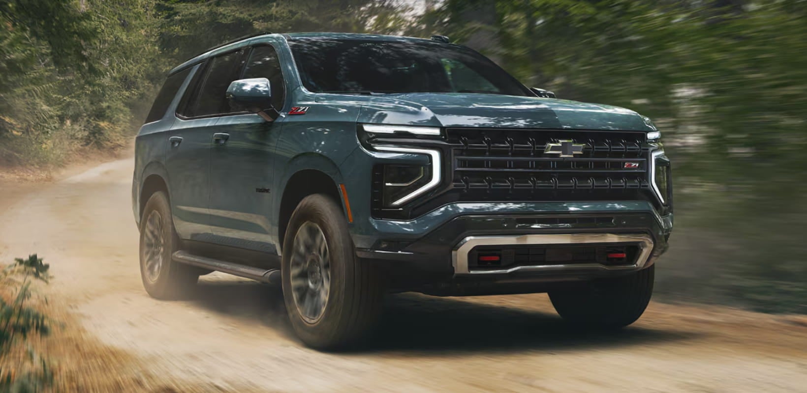 Chevrolet Tahoe driving on a dirt road through a wooded area.