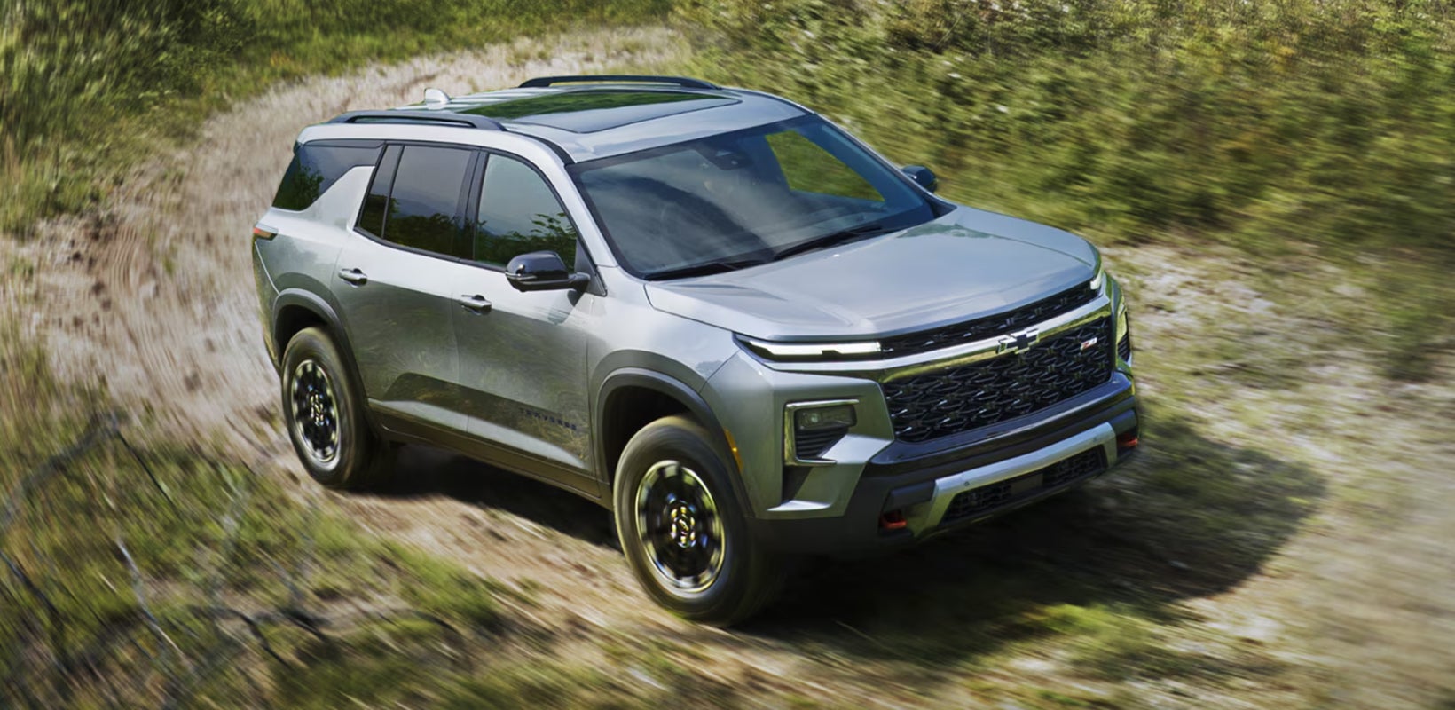 Chevrolet Traverse driving on a dirt road through a wooded area.