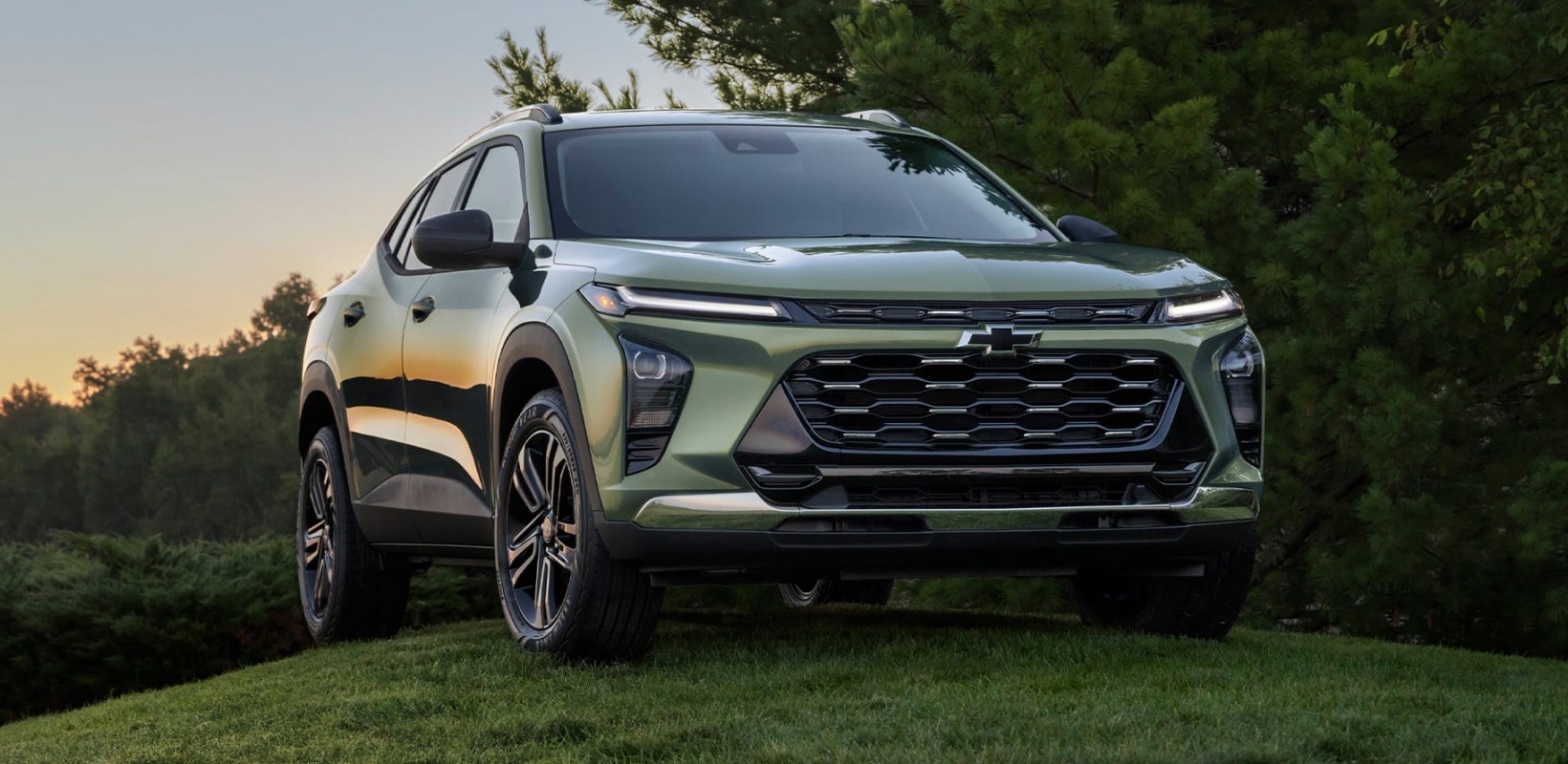 Green Chevrolet Trax parked on a grassy hill surrounded by trees.