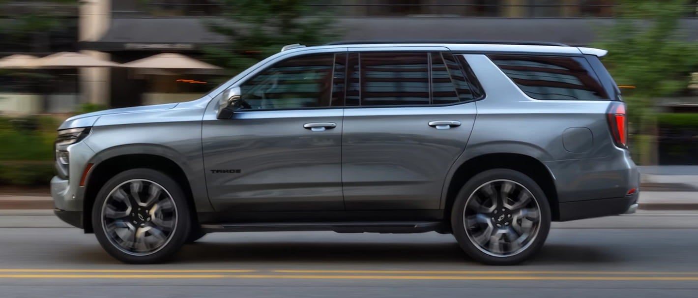 Silver Chevrolet Tahoe SUV driving along a city street, shown in side profile.