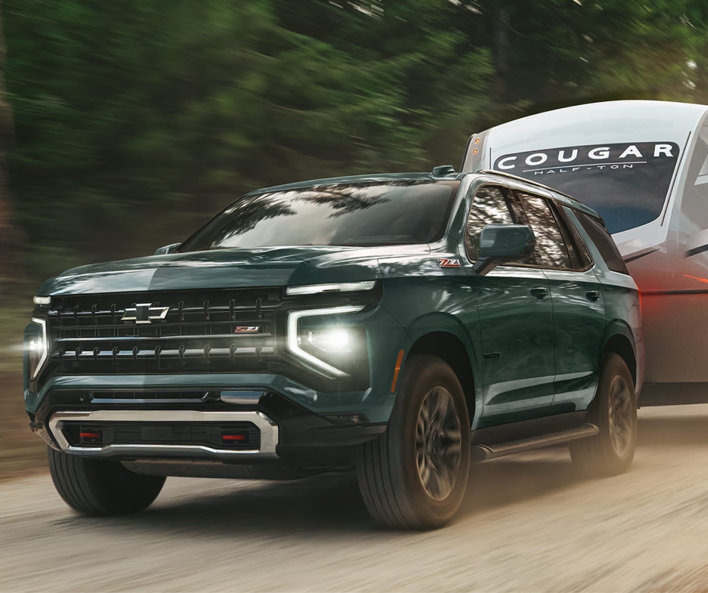 Green Chevrolet Tahoe Z71 towing a travel trailer along a forest road.